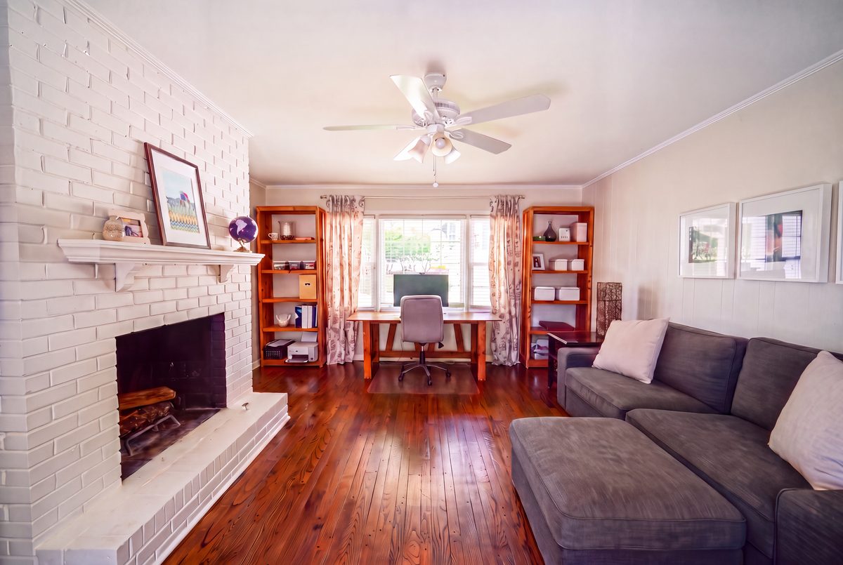 Fireside den with painted brick fireplace, built-in bookshelves, sectional sofa, and home office nook