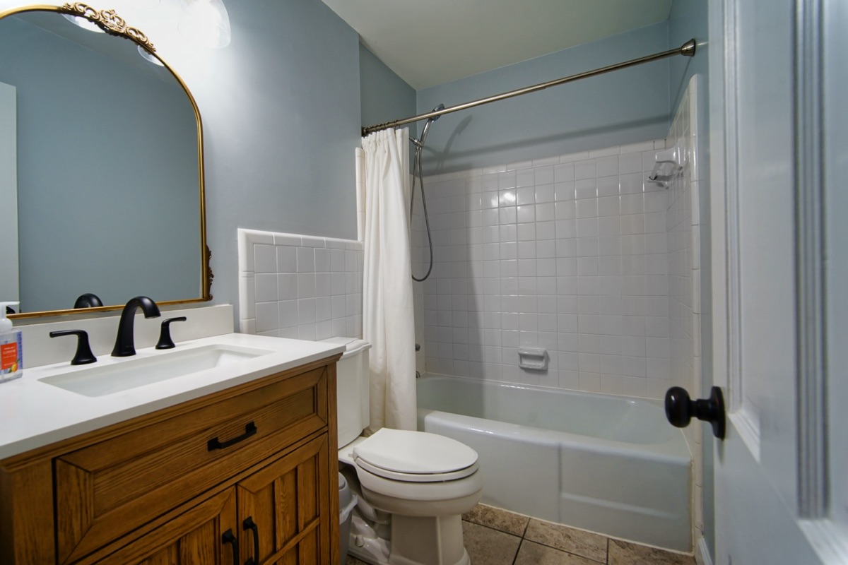 Hall bathroom with wood vanity, gold mirror, and tub-shower combo