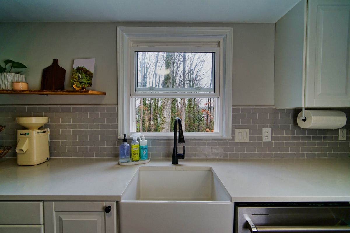 Farmhouse sink with subway tile backsplash and window overlooking trees